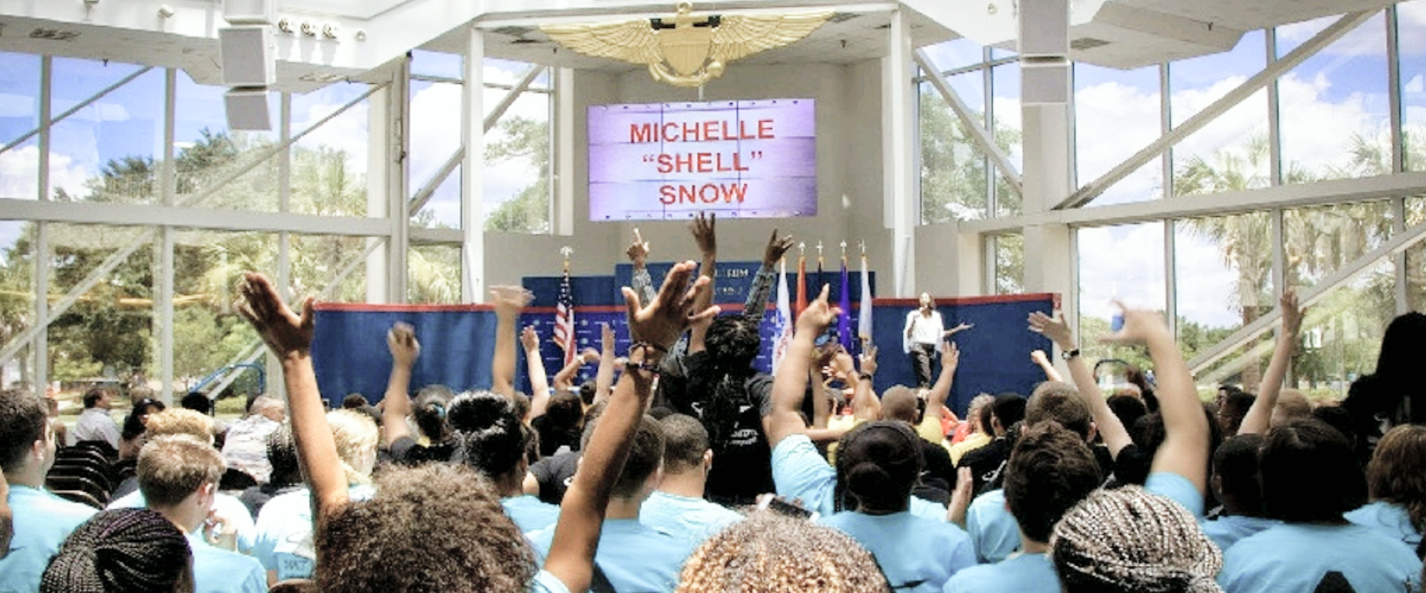 Michelle Snow on stage as a crowd raises their hands at the National Naval Aviation Museum